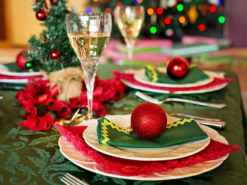 Mesa navideña, con servilletas rojas, verdes, esferas y copa de vino.